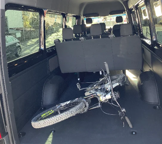 Luggage area behind the last bench of a black 9-passenger Sprinter XL with a mountain bike laid flat inside