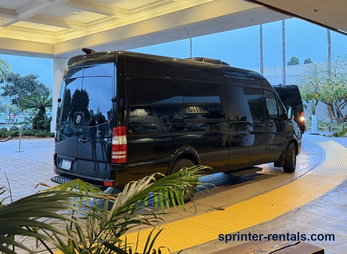 Black Sprinter passenger van picking up a group at a hotel entrance in the Anaheim area