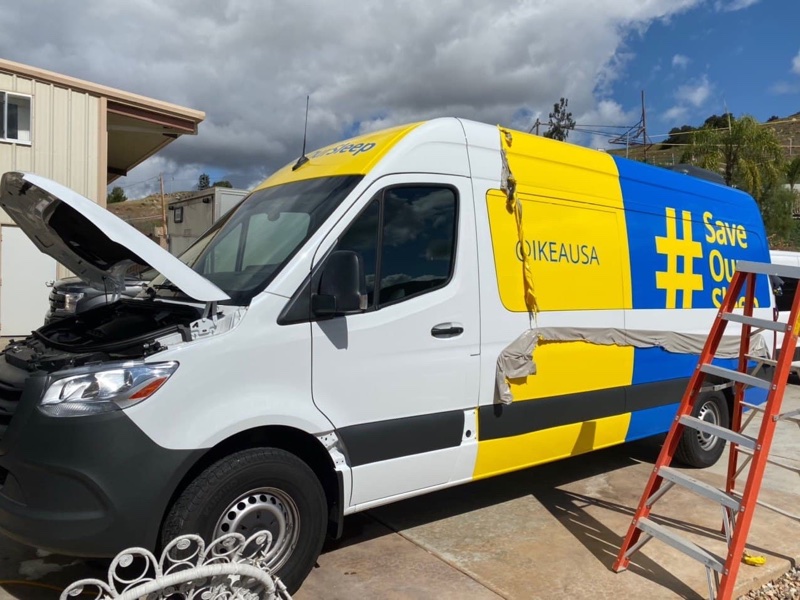 Vinyl wrap panels being installed on the side of a white sprinter van