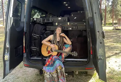 The cargo space of a rented 5-passenger Mercedes-Benz Sprinter crew van, packed with luggage and featuring a musician seated with a guitar